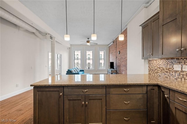 kitchen featuring tasteful backsplash, light wood finished floors, dark brown cabinets, open floor plan, and a peninsula