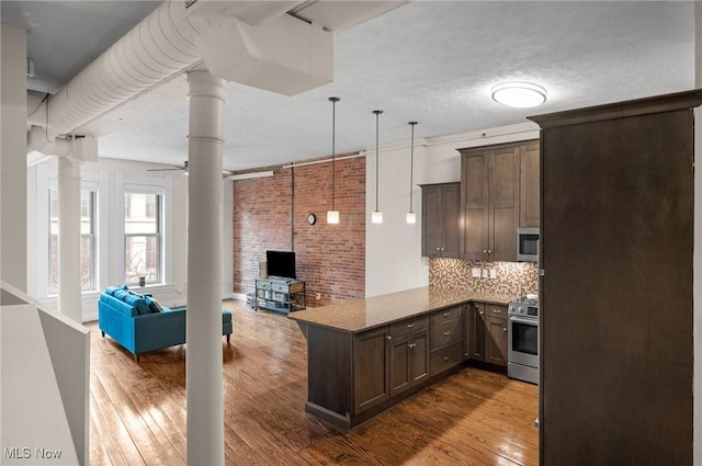 kitchen featuring appliances with stainless steel finishes, hardwood / wood-style floors, pendant lighting, dark stone counters, and kitchen peninsula