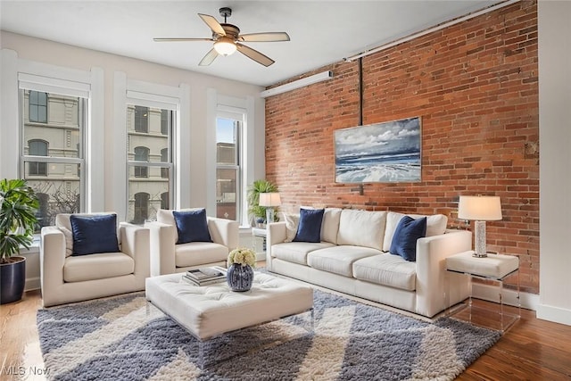 living area with ceiling fan, baseboards, wood finished floors, and brick wall