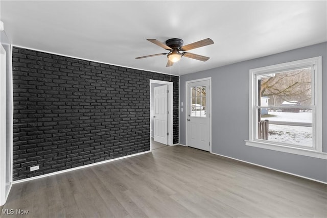 empty room featuring ceiling fan, brick wall, and light hardwood / wood-style floors