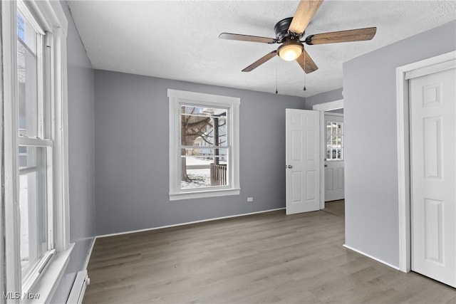 unfurnished bedroom featuring baseboard heating, ceiling fan, a textured ceiling, and light wood-type flooring