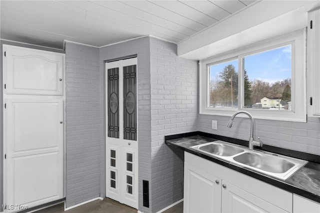 kitchen featuring brick wall, white cabinetry, sink, backsplash, and dark wood-type flooring