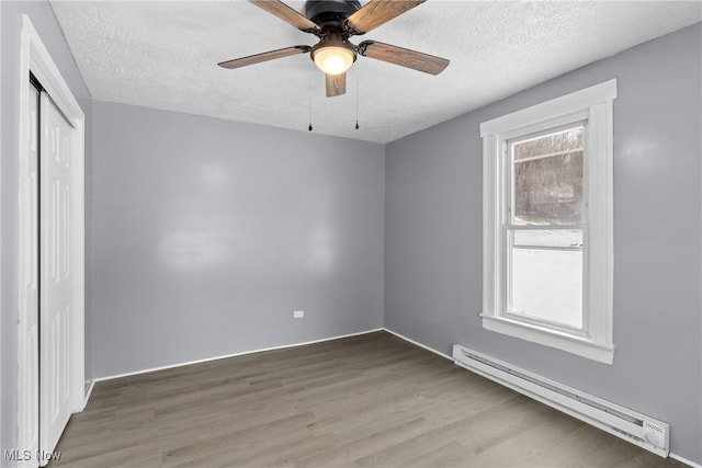 unfurnished bedroom with a baseboard radiator, wood-type flooring, ceiling fan, a textured ceiling, and a closet