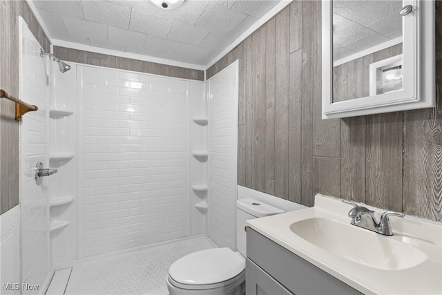 bathroom with toilet, tiled shower, vanity, and wooden walls