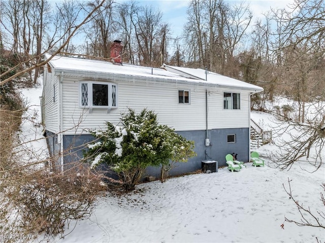 snow covered rear of property featuring central AC unit