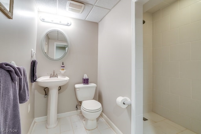 bathroom featuring a paneled ceiling, tile patterned floors, toilet, and tiled shower