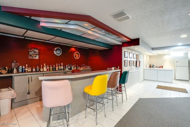 bar with white refrigerator, a textured ceiling, and light tile patterned floors