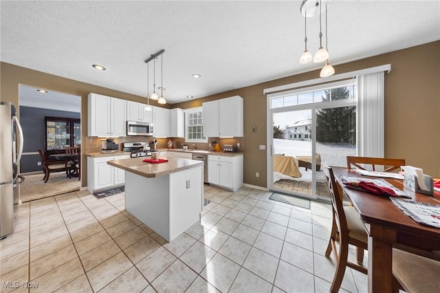 kitchen featuring a center island, hanging light fixtures, light tile patterned floors, appliances with stainless steel finishes, and white cabinets