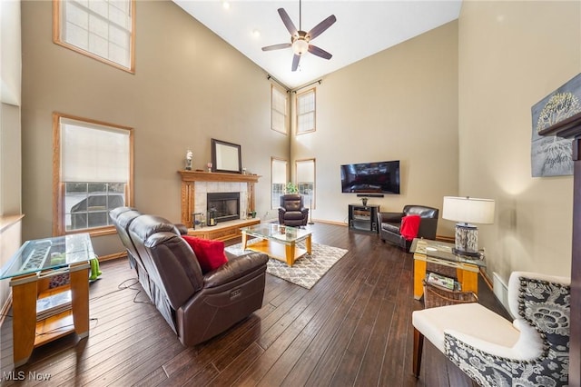 living room with ceiling fan, dark hardwood / wood-style flooring, a tiled fireplace, and high vaulted ceiling