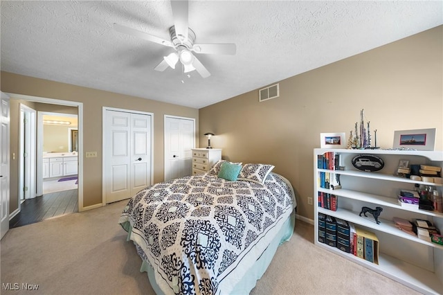 bedroom featuring ensuite bathroom, a textured ceiling, multiple closets, ceiling fan, and carpet