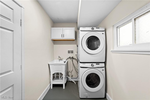 clothes washing area featuring cabinets and stacked washing maching and dryer