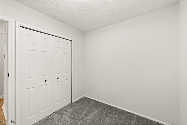 unfurnished bedroom featuring a textured ceiling, dark carpet, and a closet