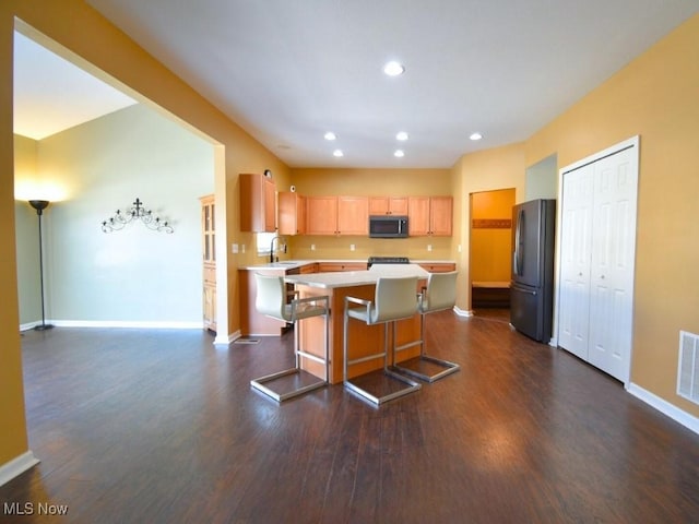 kitchen featuring a kitchen island, dark hardwood / wood-style floors, refrigerator, a kitchen breakfast bar, and light brown cabinets