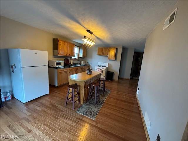 kitchen with white appliances, a breakfast bar area, hardwood / wood-style flooring, a textured ceiling, and a kitchen island