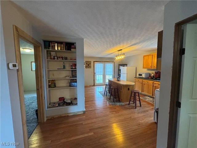 kitchen with a breakfast bar area, hanging light fixtures, hardwood / wood-style flooring, white appliances, and a textured ceiling