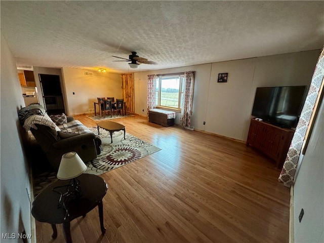 living room featuring ceiling fan, wood-type flooring, and a textured ceiling