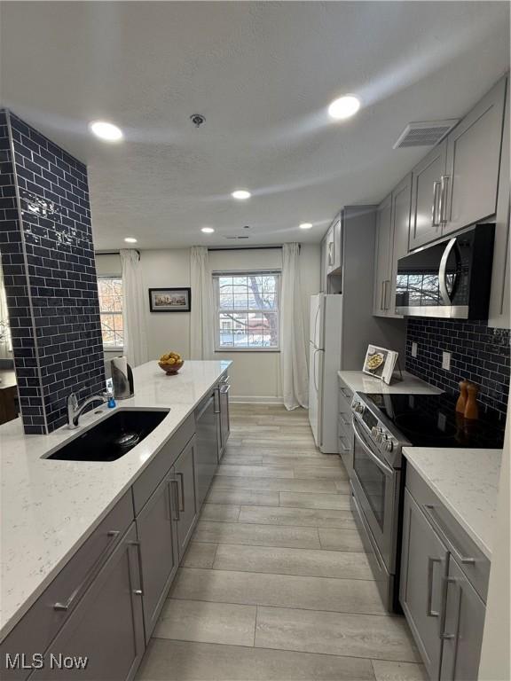 kitchen with stainless steel appliances, tasteful backsplash, sink, and light stone counters