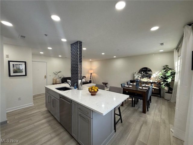 kitchen with gray cabinets, a kitchen island with sink, sink, and light hardwood / wood-style flooring