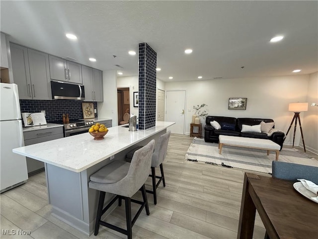 kitchen featuring gray cabinetry, a center island with sink, tasteful backsplash, and appliances with stainless steel finishes