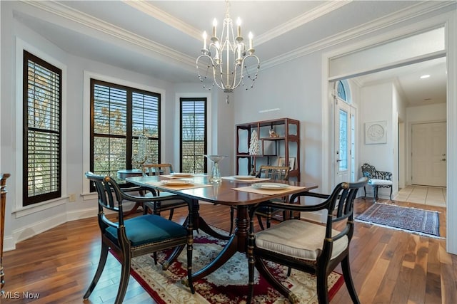 dining space with an inviting chandelier, ornamental molding, a tray ceiling, and hardwood / wood-style flooring