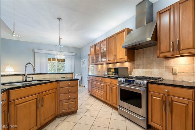 kitchen with sink, hanging light fixtures, dark stone countertops, stainless steel appliances, and wall chimney range hood