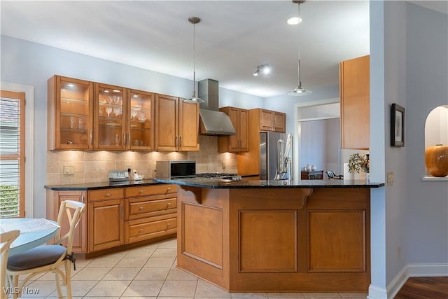 kitchen featuring decorative light fixtures, appliances with stainless steel finishes, kitchen peninsula, wall chimney range hood, and backsplash