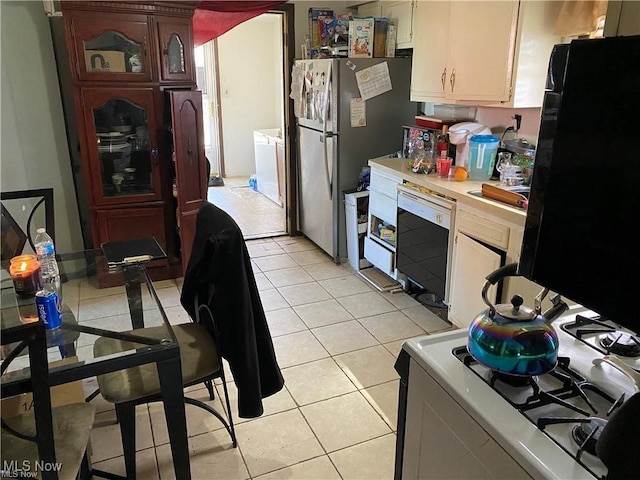 kitchen with light tile patterned flooring, dishwashing machine, stainless steel fridge, washing machine and clothes dryer, and white gas stove