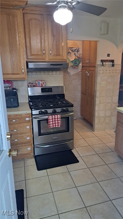 kitchen with stainless steel gas range oven, light tile patterned floors, ceiling fan, and tile walls