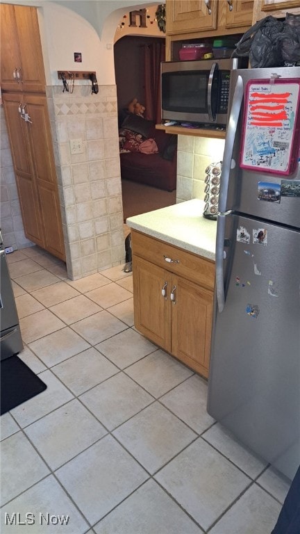 kitchen with stainless steel appliances, light tile patterned floors, and tile walls