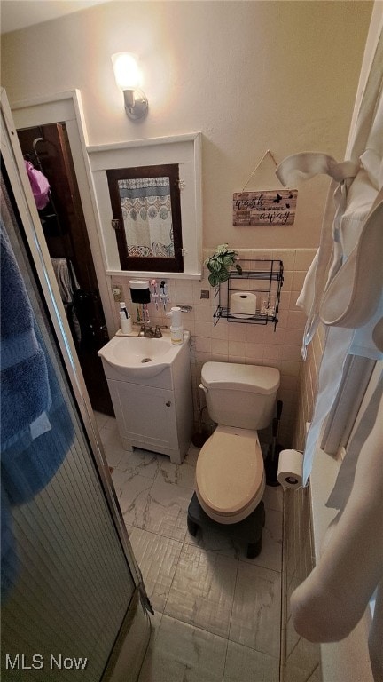 bathroom featuring vanity, toilet, an enclosed shower, and tile walls