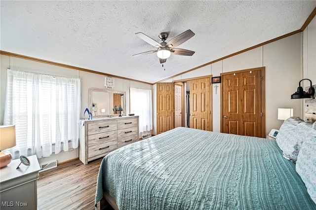 bedroom featuring ornamental molding, vaulted ceiling, a textured ceiling, and light wood-type flooring