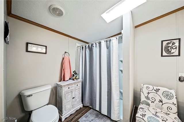 bathroom with crown molding, lofted ceiling with skylight, toilet, and a textured ceiling