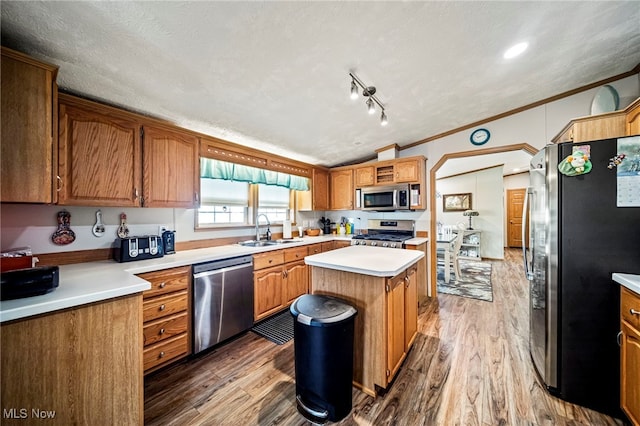 kitchen featuring sink, hardwood / wood-style flooring, appliances with stainless steel finishes, a center island, and ornamental molding