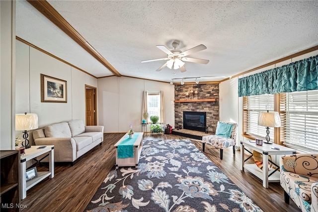 living room featuring a stone fireplace, a textured ceiling, ornamental molding, dark hardwood / wood-style floors, and ceiling fan