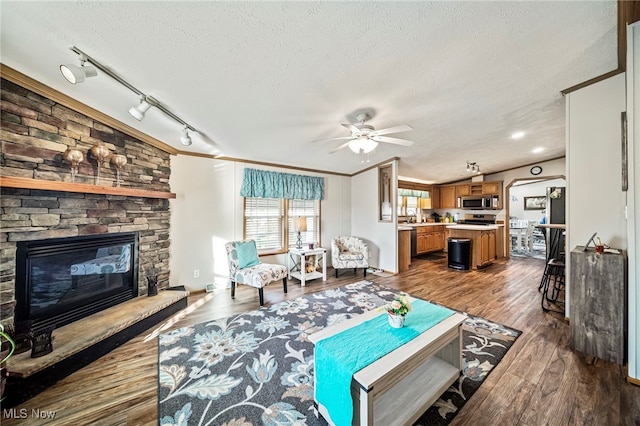 living room featuring crown molding, hardwood / wood-style flooring, ceiling fan, a textured ceiling, and a stone fireplace