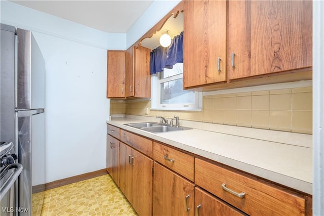 kitchen with tasteful backsplash, stove, sink, and stainless steel refrigerator