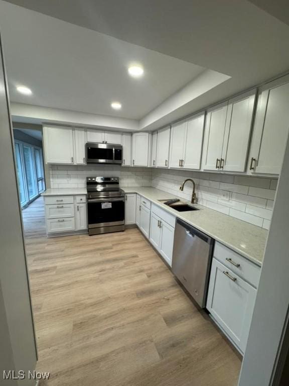 kitchen featuring sink, white cabinetry, stainless steel appliances, tasteful backsplash, and light hardwood / wood-style floors