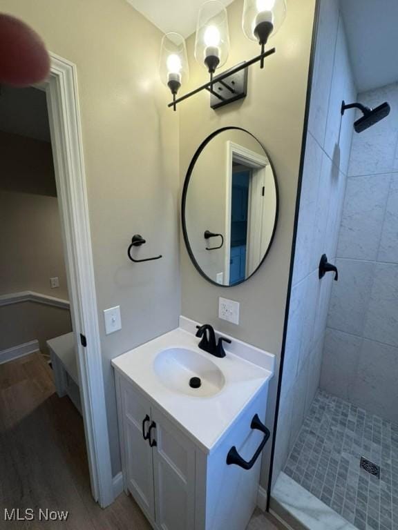 bathroom with hardwood / wood-style flooring, vanity, and a tile shower