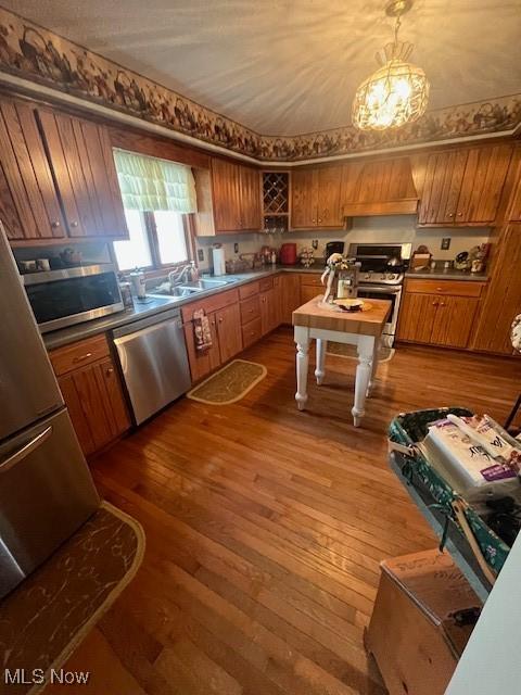 kitchen featuring premium range hood, pendant lighting, wood-type flooring, sink, and stainless steel appliances