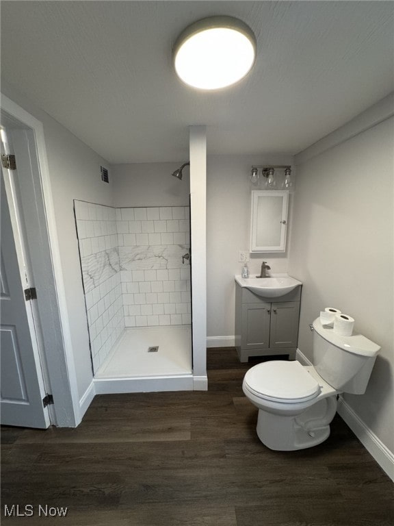 bathroom featuring hardwood / wood-style flooring, vanity, toilet, and a tile shower