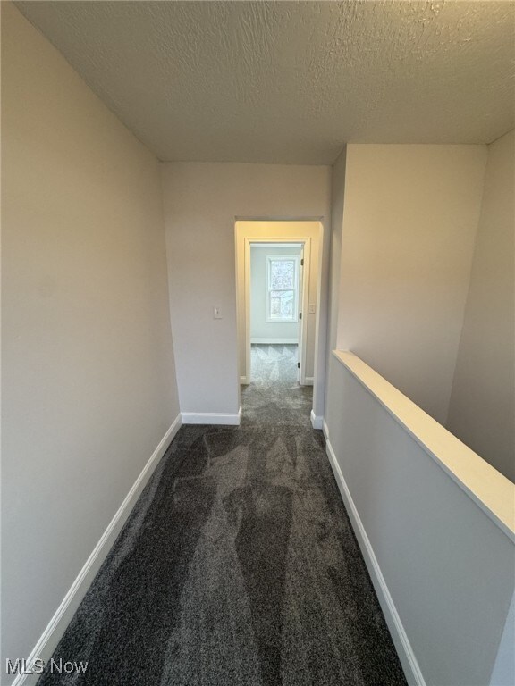 corridor featuring dark carpet and a textured ceiling