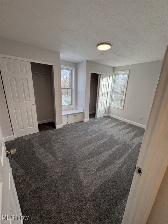 unfurnished bedroom featuring multiple windows, dark carpet, and a textured ceiling