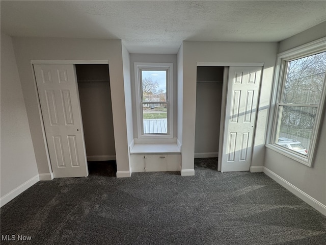 unfurnished bedroom with multiple windows, dark colored carpet, and two closets