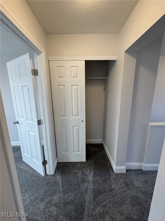 unfurnished bedroom with dark carpet, a closet, and a textured ceiling