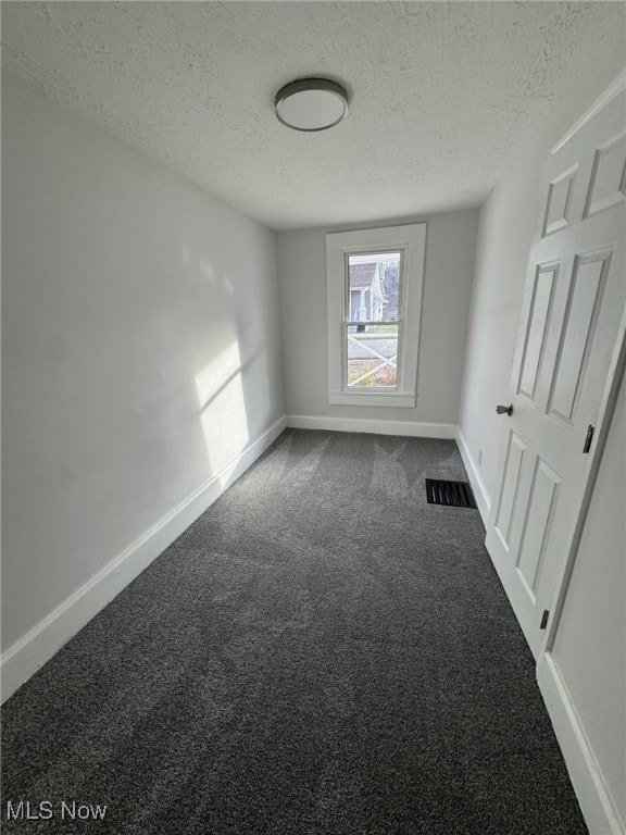 unfurnished room with a textured ceiling and dark carpet