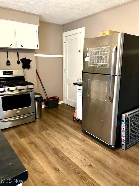 kitchen with a textured ceiling, appliances with stainless steel finishes, wood finished floors, and white cabinetry