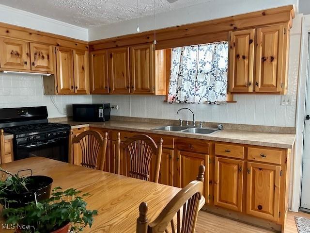 kitchen featuring sink, backsplash, black appliances, a textured ceiling, and light wood-type flooring