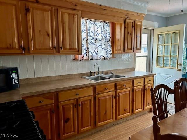 kitchen featuring tasteful backsplash, black microwave, brown cabinetry, and a sink