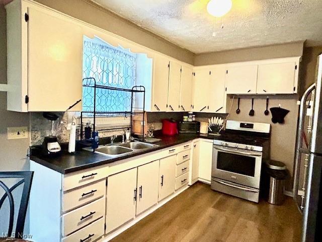 kitchen featuring dark wood-style floors, stainless steel gas range oven, a sink, and white cabinetry