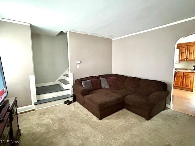 living area with arched walkways, ornamental molding, stairs, and light colored carpet